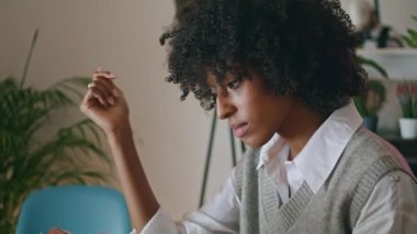 Relaxed curly girl reading book sitting at wooden table cozy home close up. Portrait of attractive african american woman enjoying literature indoors. Calm pensive lady relaxing with foliant in cafe.