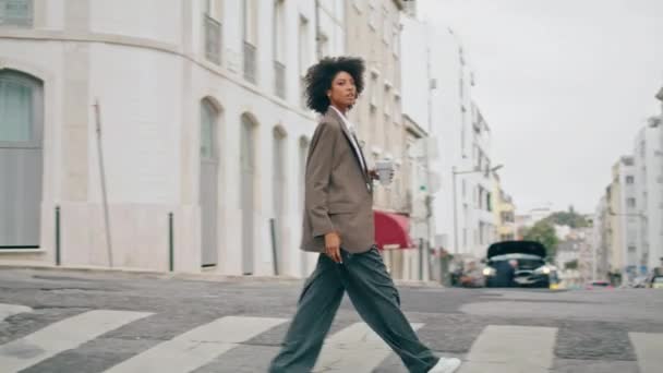 カップコーヒーを持ち帰り 美しい街を横断歩道に行く忙しい魅力的なビジネス女性 スマートフォンを持って通りを横断するアフリカ系アメリカ人女性を自信を持って 町の道を歩いている若い女の子 — ストック動画