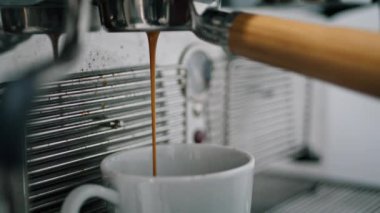 Modern professional hot drink machine making delicious fresh coffee indoors closeup. Dark tasty caffeine liquid slowly pouring in elegant white cup. Process preparing hot beverage with electric device