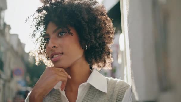 可爱迷人的女士在阳光普照的城市街道上放松地做梦 快乐的非洲裔美国女人站在室外明亮的阳光下 城镇美丽的卷曲的黑发画像 — 图库视频影像
