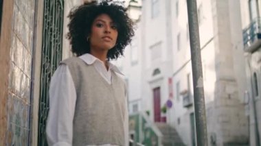 Calm relaxed woman tourist looking old city buildings walking alone summer weekend. Attractive african american girl enjoy vacation in cozy town. Pretty lady model posing camera with light smile.
