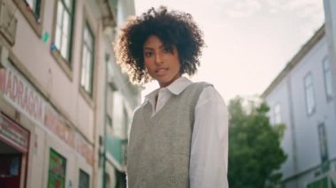 Cute attractive woman enjoy sunny weekend in city close up. Carefree african american girl standing street under beautiful summer sunlight. Relaxed young curly lady tourist walking at cozy town.