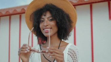 Smiling girl put sunglasses on beach vacation closeup. Happy attractive woman enjoying summer weekend at shore house. Beautiful african american look camera relaxing outdoors. Carefree holiday concept