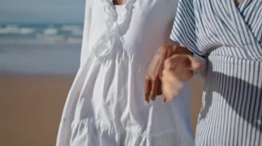 Güneş ışığında okyanus kıyısında yürüyen iki el. Kız arkadaşlar deniz kıyısında kol kola gitmenin tadını çıkarıyorlar. Tanınmayan lgbt ortakları tatilde gevşeyici konuşuyor. Çok ırklı lgbt ilişkisi