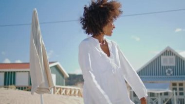 Yüzmeye giderken tişörtünü çıkaran gülümseyen kız. Neşeli Afro-Amerikan tatilini okyanus kıyısında geçiriyor. Çekici stil sahibi kadın yazları plaj evlerinde eğleniyor. Seyahat mutluluk konsepti