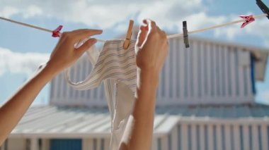 Woman hands taking swimsuit off rope closeup. Striped bikini bra air drying in summer sunlight. Unrecognized girl tourist removing underwear from dryer in vacation house. Beachwear lingerie concept.