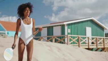 Plaj tenisçisi kız güneşli bir günde antrenman yapıyor. Zayıf ve çekici oyuncu deniz kıyısında eğleniyor. Güzel Afro-Amerikan topları yaz tatilinde dinleniyor. Hafta sonu hobi kavramı.