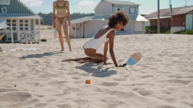 Summer girls playing tennis on sandy beach. Joyful lgbt couple resting together enjoying game at seashore in bikini. Attractive african american woman standing picking ball. Vacation fun concept.