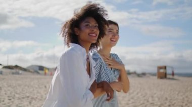 Two girls walking beach on sunny day closeup. Cheerful homosexual couple talking laughing together holding hands. Beautiful multiethnic women enjoy summer vacation at sea shore. Carefree life concept