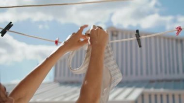 Closeup hands hanging bra at beach house. Stylish striped beachwear air drying on sunny day. Unrecognized woman tourist clipping wet swimsuit laundry after pool. Summertime vacation rest at seashore