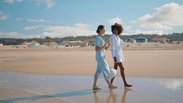 无忧无虑的女人一起去海滩 这对年轻漂亮的夫妇正在享受海滨度假 两个笑着的多文化女孩在沙滩上散步 周末无忧无虑 — 图库视频影像