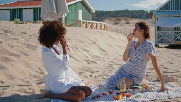 这对情侣在沙滩上拍照 两个快乐的女孩在海滩上野餐 无忧无虑的多民族美女伴侣享受暑假的照片 友谊娱乐概念 — 图库视频影像