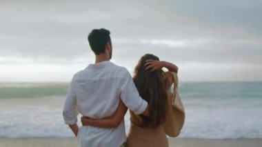Loving couple crossing ocean at evening closeup. Unknown embracing spouses enjoying wavy water. Affectionate newlyweds feeling happy spending honeymoon together. People relax at sunset sea vacation 
