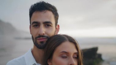 Handsome man looking camera at misty beach portrait. Smiling guy face spending honeymoon at foggy day closeup. Loving couple cuddling at ocean shore zoom on. Unshaven macho embracing wife at nature 