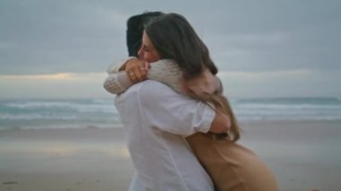 Engaged couple embracing at ocean sunset beach closeup. Brunette boyfriend swirling his cute bride at sea view place. Extremely happy woman rejoicing with fiance at evening. Marriage proposal concept 