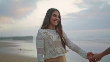 Carefree woman laughing at sunset beach date closeup. Smiling lovers walking on sea evening place. Happy girl relaxing with positive guy on ocean horizon background. Affectionate couple holding hands