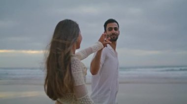 Cheerful lovers connecting hands at dark beach closeup. Smiling pair touching arms on evening ocean side. Romantic couple interlacing fingers on cloudy nature date. Loving people spend time together