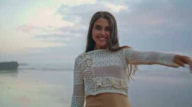 Playful girl posing water view place portrait. Cute woman stretching hand at cloudy nature closeup. Laughing lady looking camera at sandy beach. Brunette person walking at ocean horizon environment