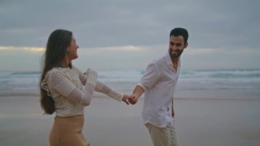 Playful pair talking dark ocean closeup. Positive lovers holding hands on evening sea coast. Romantic partners enjoying date on cloudy nature. Two loving people spend time together. Leisure concept 