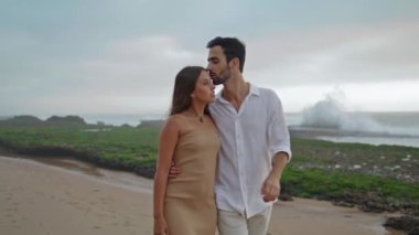 Carefree lovers walking on sandy beach closeup. Smiling man kissing positive woman tenderly on beautiful summer nature. Affectionate couple looking each other enjoying moment together on seacoast