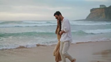 Happy lovers walking sea beach outdoors. Hispanic couple enjoying ocean coast outside. Two romantic partners going on nature date. Smiling spouses spending time together on shore. Leisure concept 