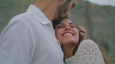 Positive woman enjoying anniversary vacation portrait. Cute lady closed eyes in unshaved man warm embrace. Bonding couple relaxing at evening beach. Ethnic lovers hugging at romantic date together