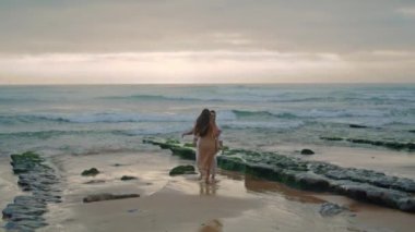 Married newlyweds having fun at wavy coastline. Cheerful man carrying pretty woman in hands. Young couple hugging in misty ocean nature. Lovely pair enjoying time together on honeymoon anniversary