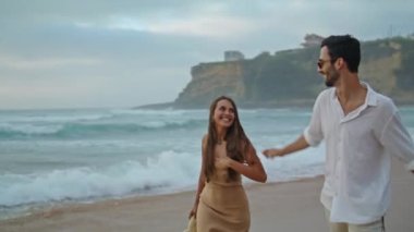 Playful pair rejoicing ocean closeup. Positive lovers holding hands on evening sea coast. Romantic partners enjoying date on cloudy sky nature. Two loving people spend time together. Leisure concept 