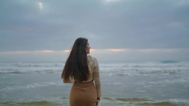 梦幻般的女人走在海浪的近处 留长发的布鲁内特模特在海滨享受日落 浪漫的女士一个人看着傍晚的海景 暴风雨冲刷着海岸 生活方式概念 — 图库视频影像