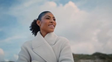 Dışarda dinlenen neşeli bir kadın portresi. Mutlu gezgin, bulutlu gökyüzüne bakan bahar haftasonunun keyfini çıkar. Güzel, sıradan bir Afrikalı Amerikalı sahilde rüya görüyor. Seyahat konsepti