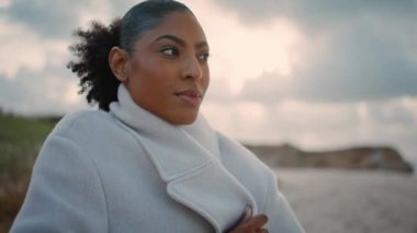 Closeup pensive african american rest cloudy shore. Black hair tourist get cold adjusting coat on autumn weekend. Thoughtful beautiful woman contemplating watching ocean. Lonely female take break. 