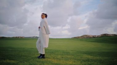 Bahar tatilinde sakin bir kadın yürüyüş alanında. Güzel, dingin bir model. Kamera bulutlu gökyüzünde yeşil çimlere çıkıyor. Dalgın Afro-Amerikan, dışarıda yalnızlığın tadını çıkarıyor. Huzurlu çayır manzarası