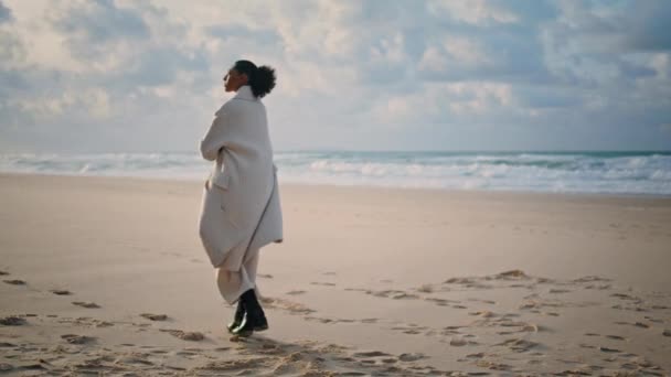 穏やかな旅行者は秋の週末にビーチを歩く 孤独なアフリカ系アメリカ人の称賛自然の波の後ろのビューを見る 平和な黒い髪の女性だけで人生を考えて時間をお楽しみください マインドフルネスバランスの概念 — ストック動画