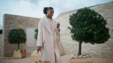 Afro-Amerikalı alışveriş torbaları taşıyor. Muhteşem başarılı kadın modern lüks malikanede yürüyor. Geriye dönüp bakınıyor ve alışveriş yapıyor. Süslü siyah saçlı kız hafta sonunun tadını çıkarıyor. Şık perakende alıcısı konsepti