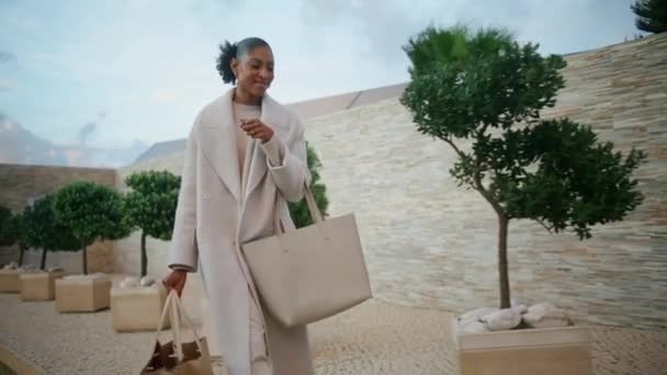 快乐的女人在街上走着购物袋 笑笑的非洲裔美国人享受周末购物回家 时尚漂亮的模特看着相机打招呼 富有的顾客带着纸袋散步 — 图库视频影像