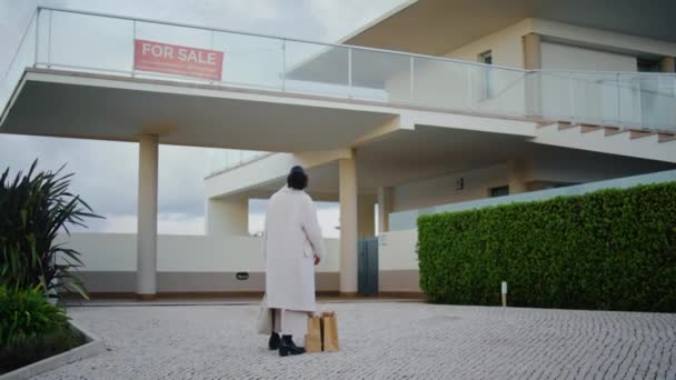 一个在郊区卖房子的女人古色古香的非洲裔美国买家正在检查附近的现代豪宅 有重点的黑发经纪人在大楼等着 贷款抵押概念 — 图库视频影像
