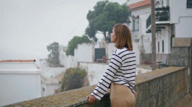 Güzel bir turist yaz tatilinde kasaba manzarasının tadını çıkarıyor. Gülümseyen kız Avrupa gezisinde resimli eski beyaz yıkama mimarisine hayran poz veriyor. Kaygısız romantik kadın tarihi köyü keşfediyor..