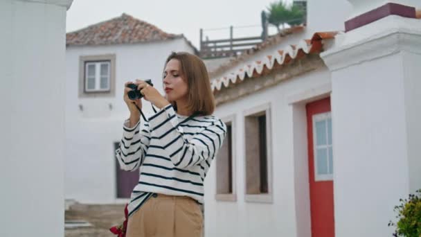 少女は古い町を歩いて旅行写真を作る 夏休みに古いカメラで写真を撮る街を探索する美しい観光客 笑顔の女性写真家のチェックショットを離れて行く 農村観光レジャー — ストック動画