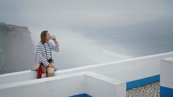 在美丽的海滨景色下喝着咖啡的游客放松了 女孩喜欢一个人在静坐的白色屋顶上度假 漂亮的街头摄影师欣赏风景 一路平安 — 图库视频影像