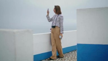 Turist deniz kenarında tatil fotoğrafları çekiyor. Güzel blogcu yaz gezisinde sosyal medya için içerik yaratıyor. Akıllı telefon kullanarak deniz manzarasının tadını çıkaran rahat bir kız. Avrupa yolculuğu anıları kavramı.