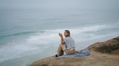 Huzurlu kadın okyanus kıyısında müzik dinliyor. Deniz kıyısı pikniğinde dinlenen, deniz dalgaları manzarasında en sevdiği podcastın tadını çıkaran bir kız. Güzel bir turist taze hava soluyor..