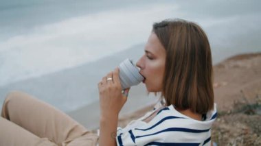 Okyanus manzaralı kahve içen bir kız. Gevşemiş turist dinlenme kenarı yaz haftasonu sıcak sabah içeceğinin tadını çıkarıyor. Huzurlu bir kadın uzanmış, tatilde dinleniyor. Deniz kıyısı sakinleşme konsepti