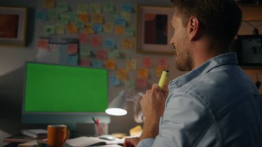 Evdeki iş yerinde şarkı söyleyen komik insan, yakın plan. Gülümseyen ve müzik dinleyen bir öğrenci yeşil ekran akşam kuşağında oynaşıyor. Pozitif serbest çalışan, gece evinde eğleniyor.