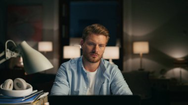 Karanlık iç mekanda masaüstü okuma yapan olumlu bir adam. Uzak bir iş yerinde sunum izleyen hoş insana yakınlaş. Evde yalnız oturan gülen adam Webinar 'ı dinliyor. Akşam yaşam tarzı