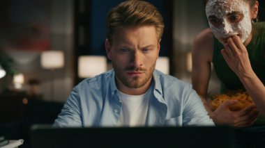 Odaklanmış adam okuma cihazı akşam yakın planda. Abur cubur yiyen sinir bozucu kadın bilgisayar ekranını işaret ediyor. Düşünceli bir adam ev hanımına dikkat etmez. Serbest Çalışan Bilgisayarı uzaktan tarıyor