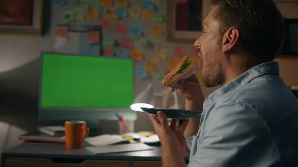 饥饿的学生在晚间房吃三明治 有胡子的人晚上说话时不认识的对话者 积极的人在凌乱的家庭工作场所观看模拟台式计算机 — 图库照片