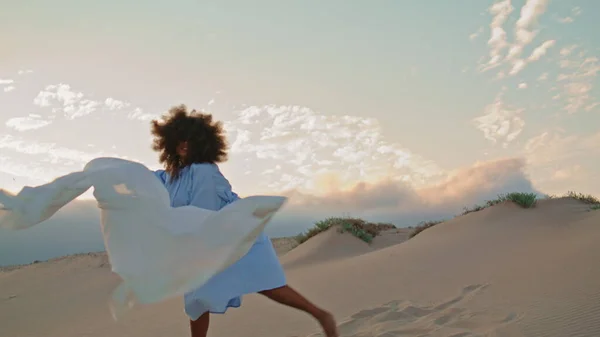 Dancer performance with fluttering white cloth in beautiful desert summer haze. Passionate african american woman waving light fabric on wind dancing modern style. Sensual girl moving on sand dunes.