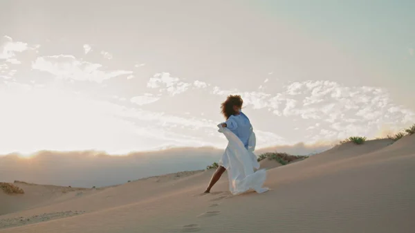 有才华的年轻姑娘在落日的天空中 在沙漠中 与飘扬的白布共舞 卷曲的非洲裔美国女人优雅地举着轻薄的布 吹着夏日的寒风 舞蹈概念 — 图库照片