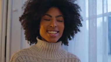 Perde arkasında gülümseyen neşeli bir kadın. Kıvırcık saç stili pozitif kadın akşam dairesinde mutlu görünüyor. Afrikalı neşeli kız pencereye bakıyor. Keyifli bir hafta sonu geçiriyor. 