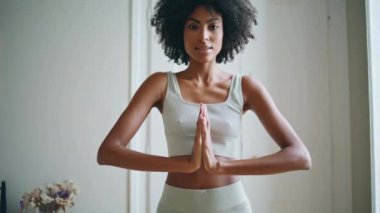 Huzurlu kadın namaste evde yakın çekim yapıyor. Kıvırcık pozitif bir kadın, beyaz iç mekanda meditasyon yaparken ellerini birleştiriyor. Huzurlu Afro-Amerikan modeli yoga gevşemesi uyguluyor. Formda kız uyum içinde. 